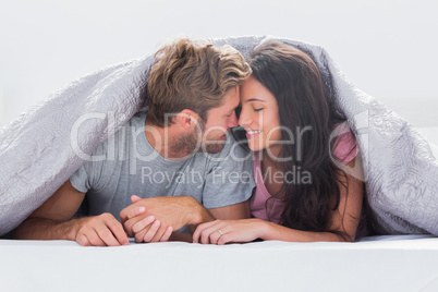 Cheerful couple head against head under the duvet