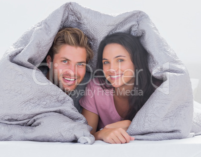 Cheerful couple wrapped in the duvet
