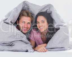 Cheerful couple wrapped in the duvet
