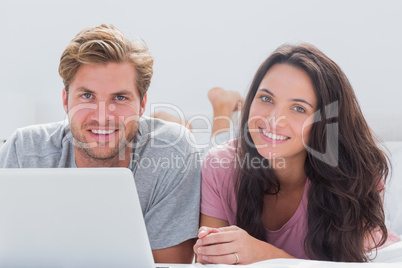 Cheerful couple using laptop in bed