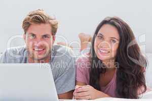 Cheerful couple using laptop in bed