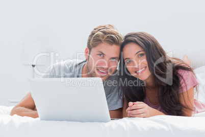 Cheerful couple with laptop in bed