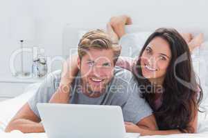 Happy couple with a laptop in bed