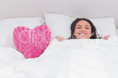 Woman lying in bed next to a fluffy heart pillow