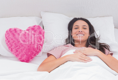 Woman lying in her bed next to a pink heart pillow