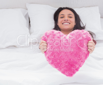 Woman in her bed holding a fluffy heart cushion