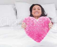 Woman in her bed holding a fluffy heart cushion