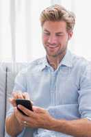 Cheerful man using his smartphone on a couch