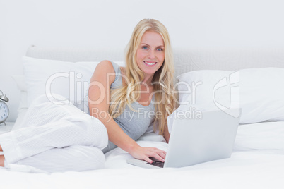 Woman using her laptop laid on her bed