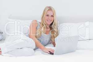 Woman using her laptop laid on her bed