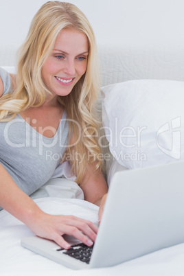 Woman typing on her laptop on her bed