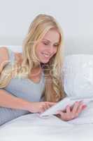 Cheerful woman touching her tablet in bed