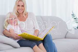 Mother and daughter sitting on couch reading a book