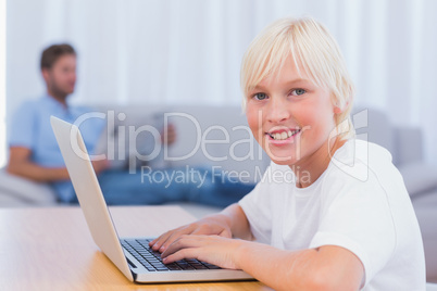 Little boy using laptop while his father is reading on the couch