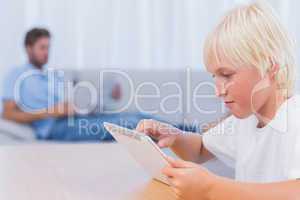 Boy using tablet pc while his father is reading