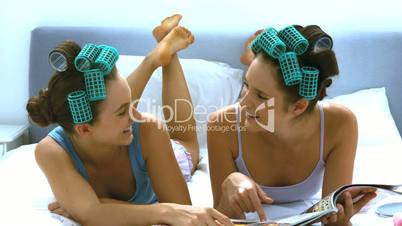 Friends with hair roller laughing and reading a tabloid
