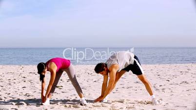 Sportsman and sportswoman stretching on the beach