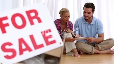 Delighted couple sitting on floor using tablet