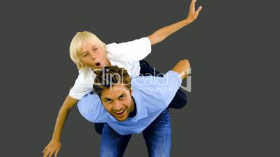 Son having a piggy back on his father on grey background