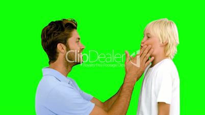 Man pressing inflated cheeks of his son on green screen