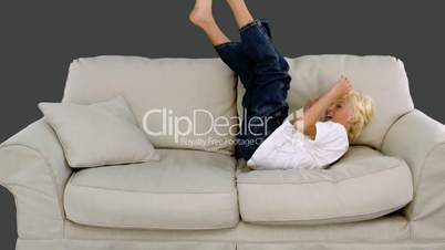 Young boy jumping on the sofa on grey background