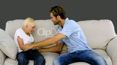 Father tickling his son on the sofa on grey background