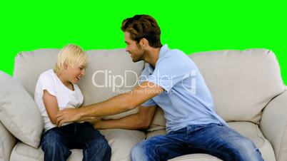 Father tickling son on the sofa on green screen