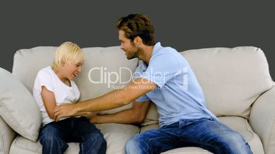 Father tickling son on the sofa on grey background