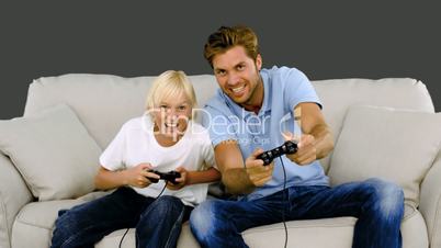 Father and son playing video games on the sofa on grey background