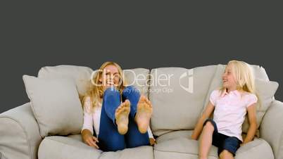 Mother and daughter jumping on the sofa on grey background