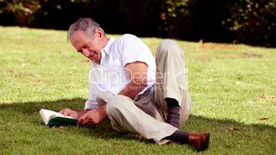 Mature man laying on the grass and reading a book