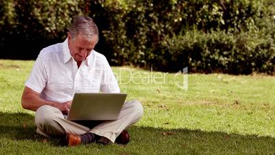 Mature man sat on the grass using his laptop