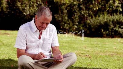 Mature man sat on the grass using his tablet computer