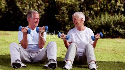 Mature couple sat on the grass lifting dumbbells