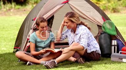 Mother and daughter reading a book in front of their tent