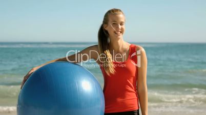 Happy woman holding gym ball on the beach