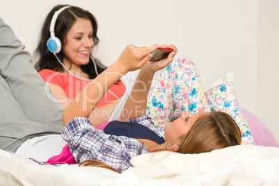 Teen girls relaxing on bed checking phone