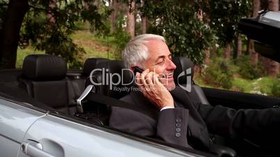 Happy businessman phoning in his convertible car