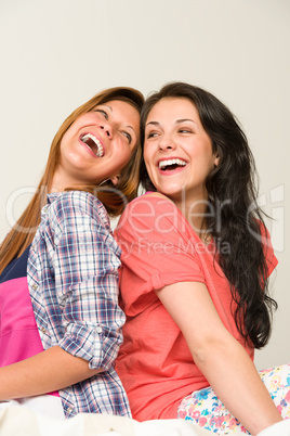 Playful friends sitting back-to-back and laughing