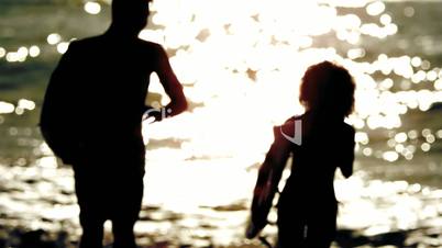 Silhouettes of friends holding surfboard and running on the beach