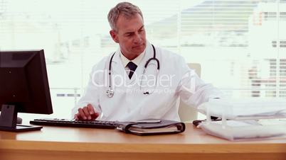 Doctor picking up the phone and using his computer