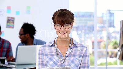 Cheerful designer posing while her colleagues are working together