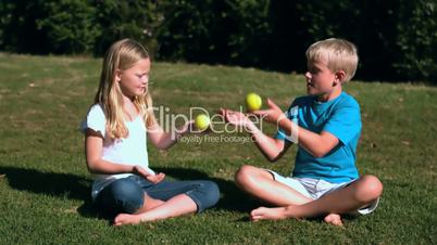 Siblings sat in a park playing with tennis balls