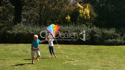 Little girl running after her brother playing with a kite