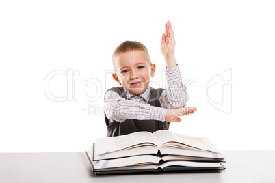 Child with books at desk gesturing hand up for answering school