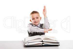 Child with books at desk gesturing hand up for answering school