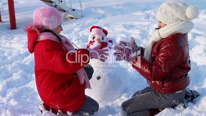 Happy girls playing a game in front of a snowman