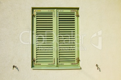Closed green shutters on a bright yellow wall.