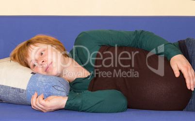 Pregnant woman lying on a sofa thinking