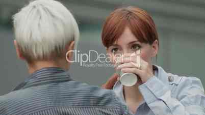 Two friendly businesswomen chat and drink during coffee break